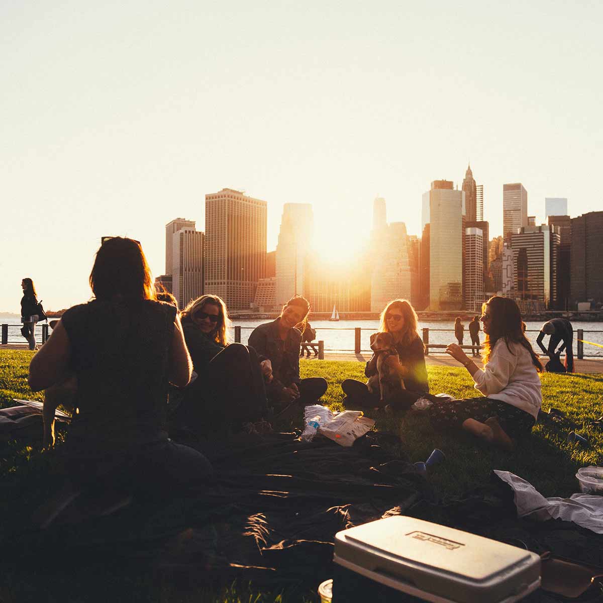 outdoor activities with group of people sitting near water with skyline and sunset in background