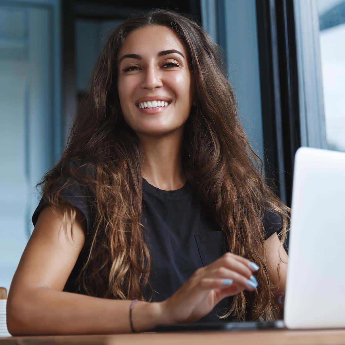 Woman Smiles At Camera While Working On A Computer.